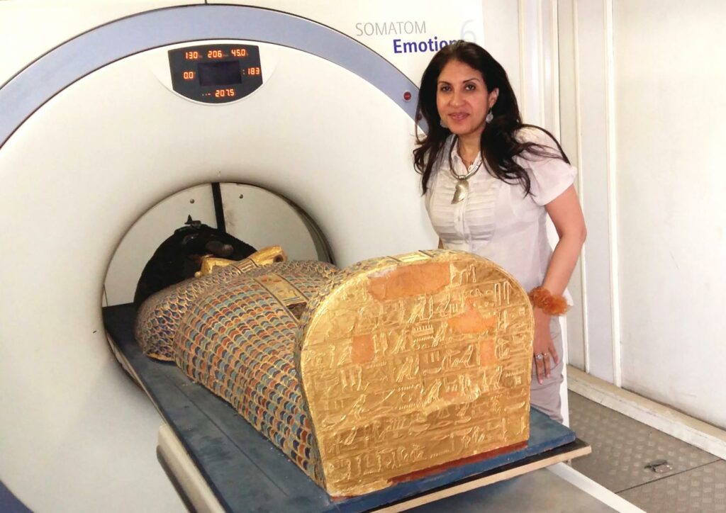 Dr. Sahar Saleem steht neben der Mumie, welche soeben in den CT Scanner hineingefahren wird.
