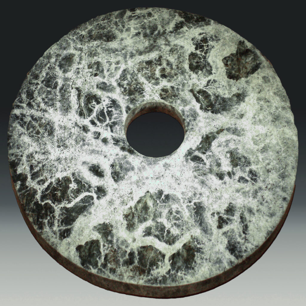 Jadescheibe der Liangzhu-Kultur, deren gleichnamige Hauptstadt zu den 100 wichtigsten archäologischen Funden zählt. Die Scheibe hat in der Mitte ein schmales Loch und besteht aus schwarzem Gestein mit dicken weißen Adern.