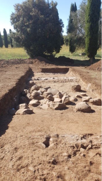 Das Foto zeigt den Grabungsschnitt, in dem sich Reste der antiken Via Latina befinden. Zu sehen sind mehrere Ansammlungen von Steinen, die das antike Straßenpflaster bildeten.