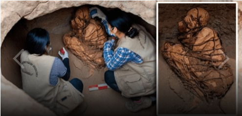 Das Bild zeigt zwei Archäologinnen, die die Mumie aus der Prä-Inka-Zeit, die von Sand bedeckt war, freilegen. Die Beine der Person liegen eng am Körper, die Hände sind vor dem Gesicht gefaltet. Der ganze Körper und der Kopf ist in ein dickes Seil gewickelt.