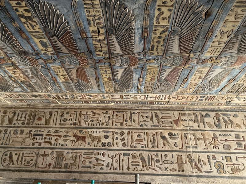 Zu sehen ist ein Architrav im Tempel von Esna, der mit Hieroglyphen versehen ist. Die Decke ist mit einem fliegenden Geier geschmückt unter dessen Klauen sich jeweils Hieroglyphen befinden.