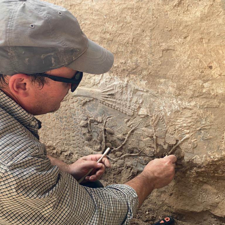 ein Mann säubert mit einem Pinsel ein Steinrelief in Ninive