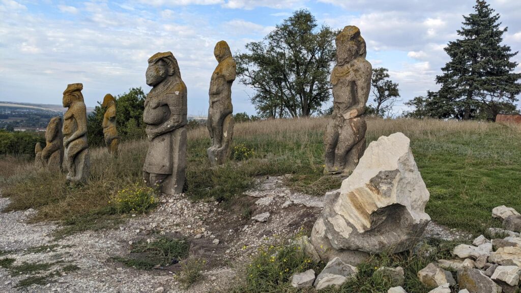 Mittelalterliche Steinskulpturen aus dem Gebiet Charkiw in der Ukraine. Zu sehen sind sechs Figuren stehender Menschen, im Vordergrund sind zerbrochene Steine.
